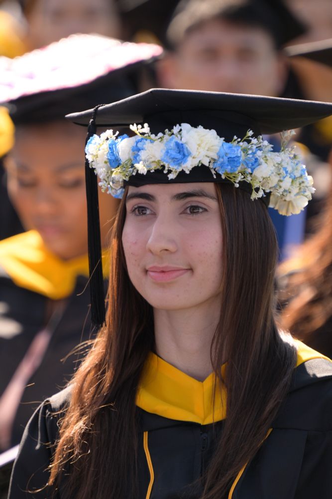 Graduate wearing a flower crown of white and blue blossoms around the base of her cap.