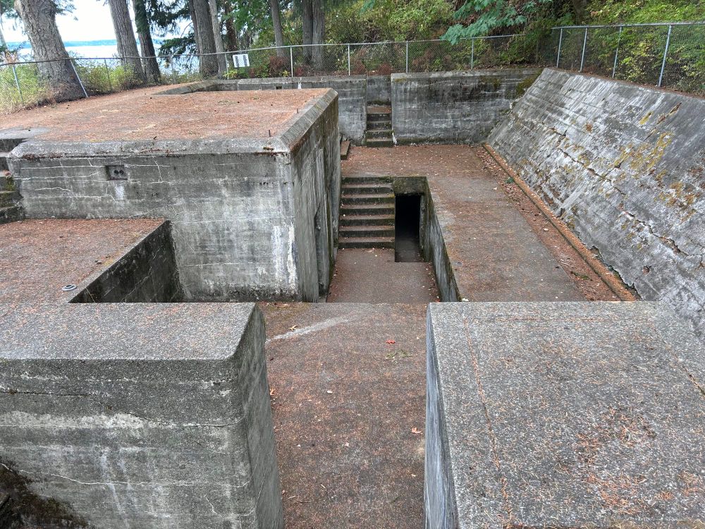 old battery originally intended for use against mines in the bay. there used to be guardrails and a structure on the upper left concrete platform with metal rods sticking out of it(the doors on that wall lead to the munitions area). it’s an old and small concrete labyrinth, at least when you first look at it. there are stairs and steep walls, and a dark doorway that leads to a shelter. you could split this structure down the middle(horizontal with this pics orientation), and it would be a perfect mirror on each side.
the fence has a caution sign warning of potential hazards, but you’re allowed to explore at your own risk. 