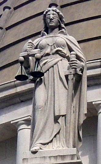 Justice stands, blindfolded, with scales in one hand and a sword in the other. 