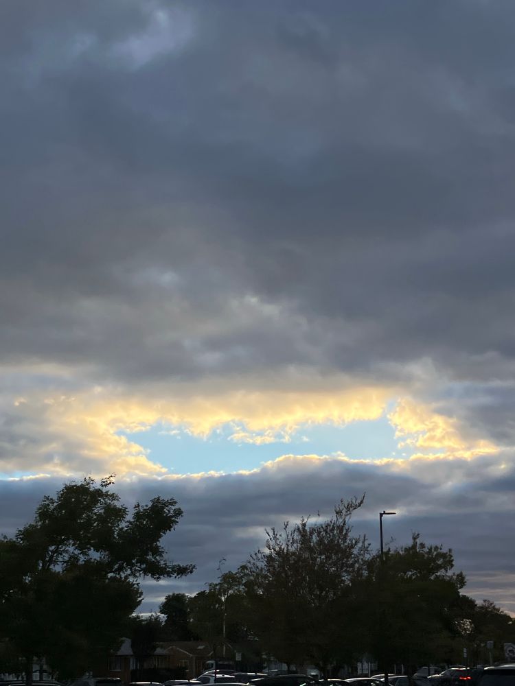 Parallelogram-shaped opening in the clouds, lit yellow by sunlight