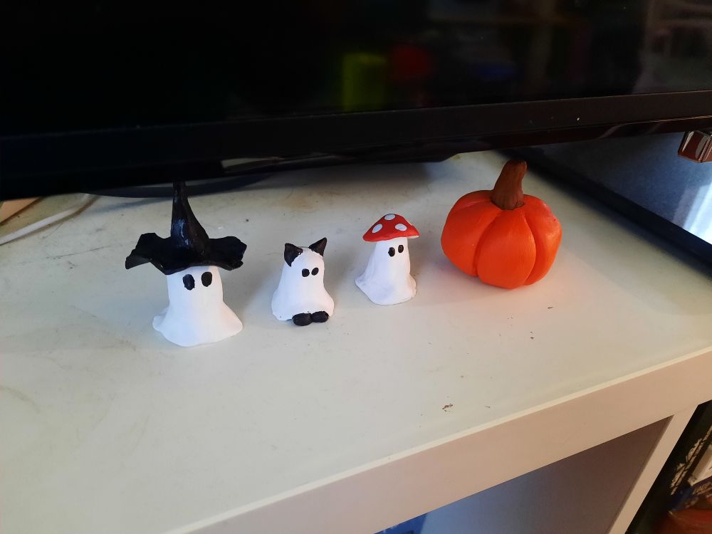 3 petits fantômes (l'un avec un chapeau de sorcière, l'autre avec des pattes et oreilles de chat, le dernier avec un chapeau de champignon) et une citrouille faits en argile et peints