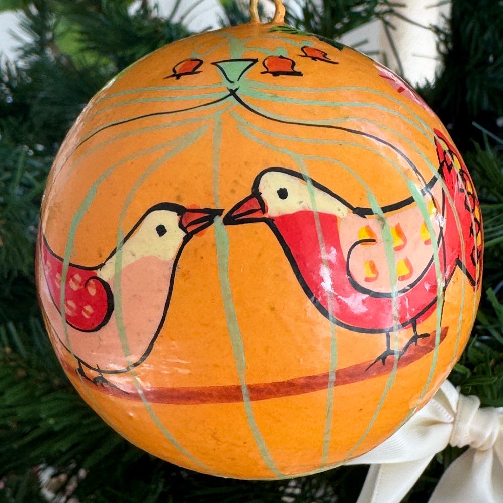 The background of this ornament is orange. It has two birds facing each other in a cage that is green bars. The turtle doves are white, pink, red and orange, and they are standing on a stick swing.