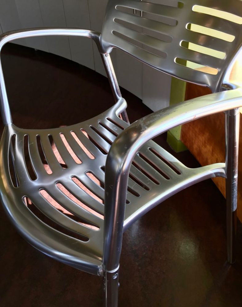 A stainless steel chair that has not only smooth, brushed stainless steel, but also smooth curved lines in its design. The chair has smooth, rounded slats in the seat and back that allow some color to come through.