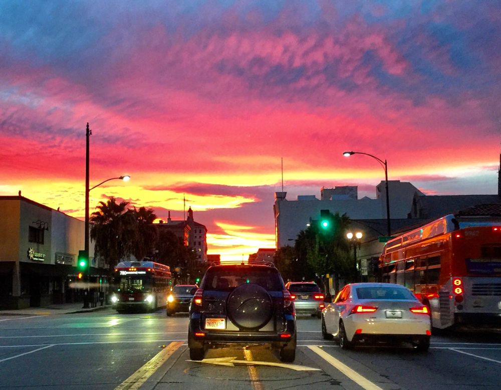 Image taken while I was sitting at a traffic light going home from work at sunset. The sky is ablaze with color...yellow, pink, red, purple, blue. Drivers have their headlights on. This is Colorado Blvd in Pasadena, a main artery there. 