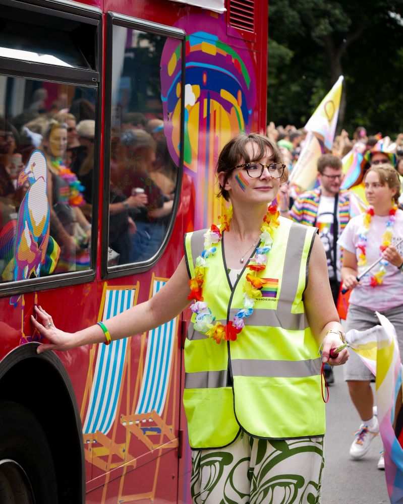 Photo showing a person holding a pride flag walking next to a Brighton & Hove bus.