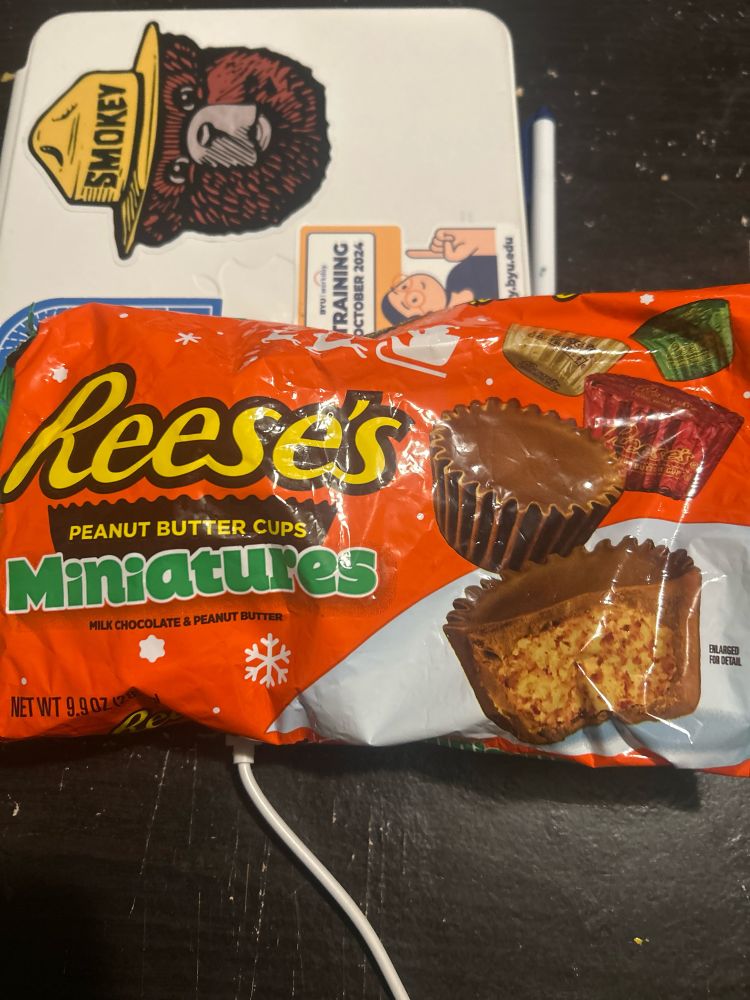 An opened bag of Reese’s Peanut Butter Cups rests on top of a computer tablet case. 