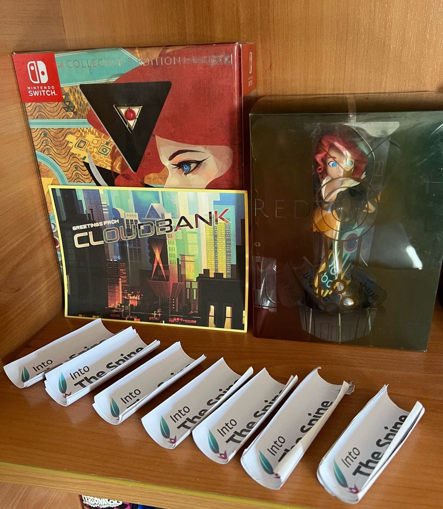 a postcard of cloudbank, a collectors edition of transistor, and a figure of red sit on a shelf behind 7 stacks of into the spine stickers 