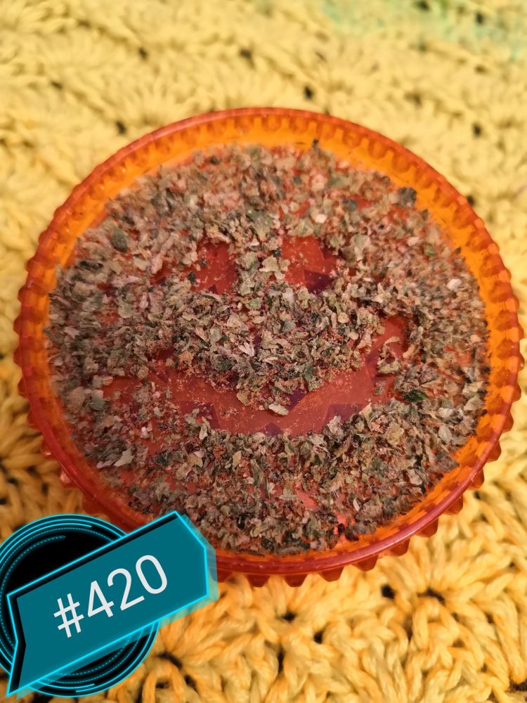 Grinder, gefüllt mit gemahlenem Gras. Darin ein Smiley und #420
