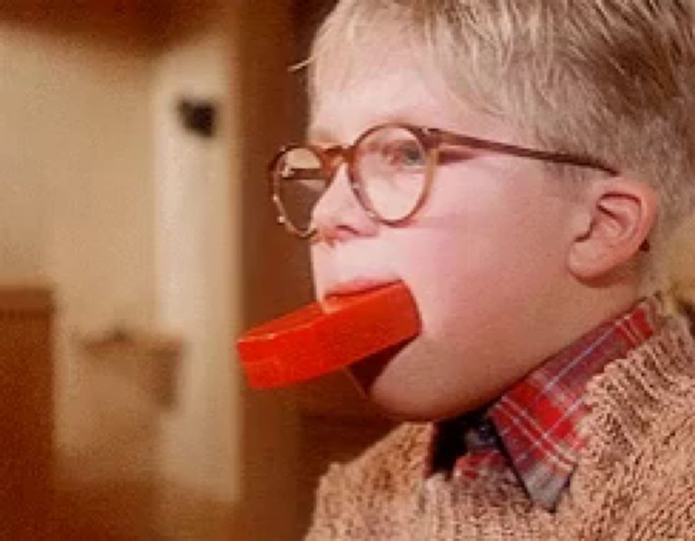 a young boy wearing glasses is eating a red candy bar .