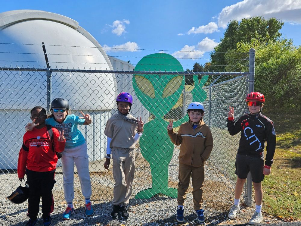 Five of Sunday's 29 alumni adventurers join a friendly green alien sculpture in showing the peace sign beside an observatory at a Belleville, Illinois, school.