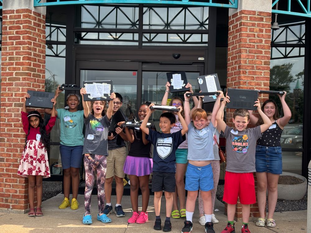 Eleven newly minted Earn-A-Computer camp grads raise their Linux laptops over their heads in triumph at the entrance to SLPL's Divoll library branch on the north side.