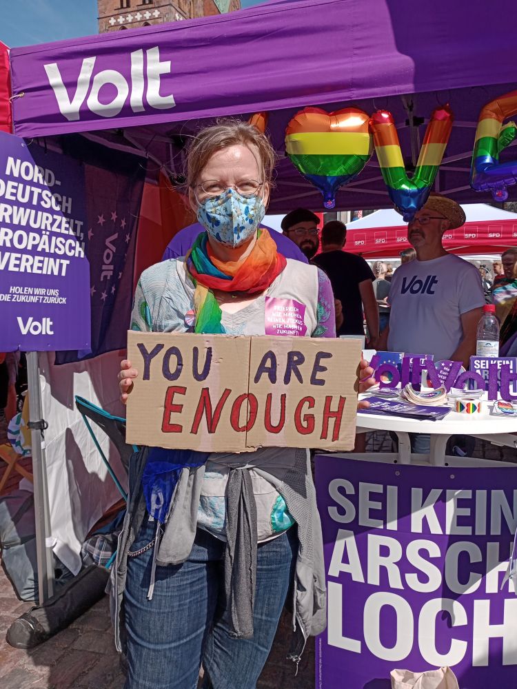 Eine Frau mit Maske hält ein Demoschild auf dem steht: You are enough 