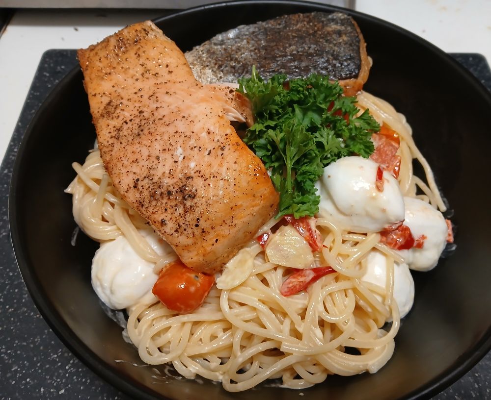 Schale mit Spaghetti in Sahne geschwenkt mit Red Hot Peperoni, Knoblauch, Cherrytomaten, Bueffelmozzarella dazu auf der Haut gebratete Lachsfilets, Petersilie.