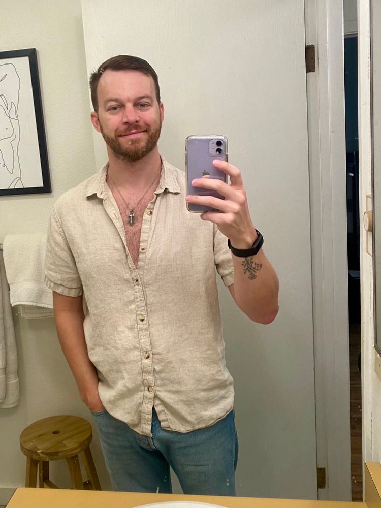 Mirror selfie in a linen shirt and jeans, with a gem pendant necklace