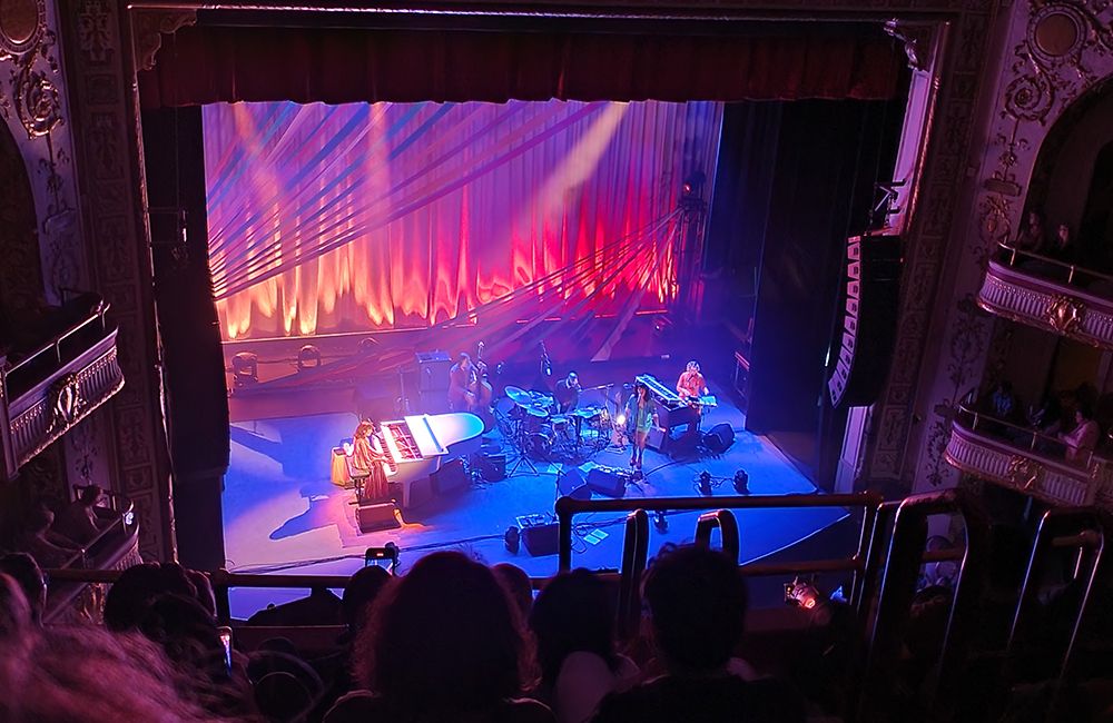 Nora Jones seated at a white piano on stage with her band at the Apollo Theater in Harlem during a concert in May 2024.