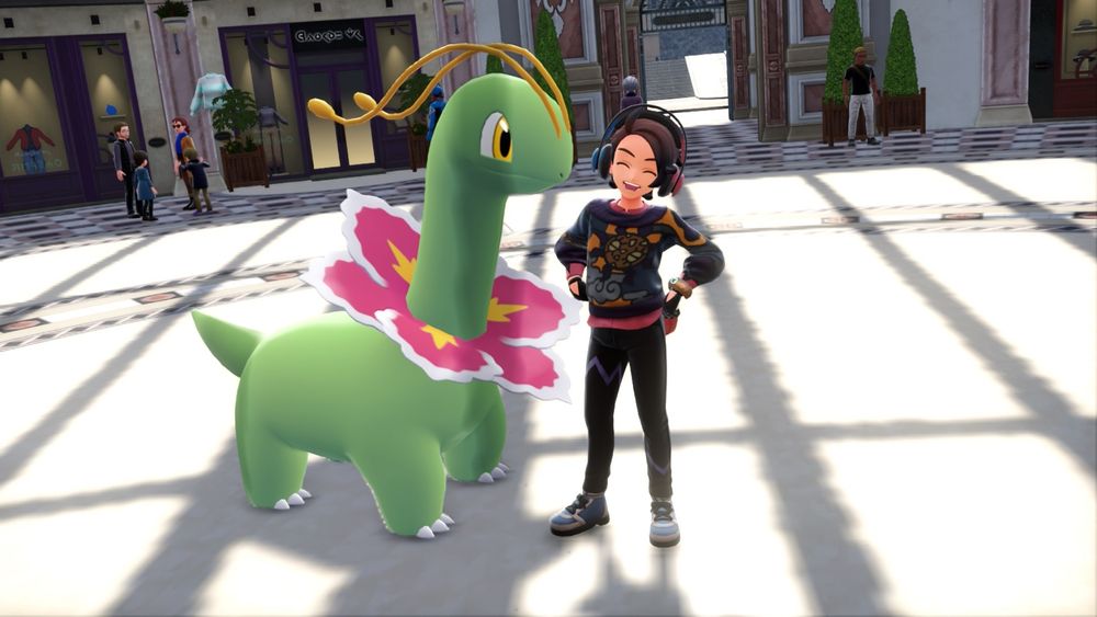 A screenshot from the video game, Pokémon Legends Z-A, featuring a Meganium and their trainer inside a large shopping plaza. The trainer is smiling at the camera, with large blue & red headphones, a sweatshirt featuring Solrock, stylish gloves, and tight black pants with a blue chevron on each pant leg.