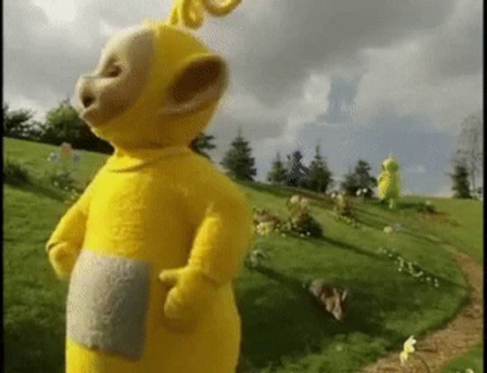 a yellow teddy bear is standing on top of a grass covered hill .