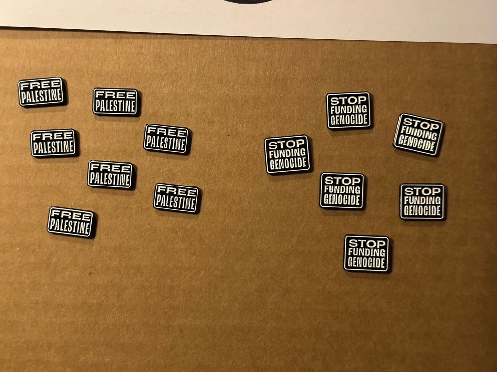 Small enamel pins, some say “Free Palestine” while others say “Stop Funding Genocide”