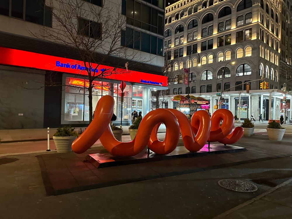 Large red sculpture on NYC street, spelling “love” in 3D, tubular lowercase cursive 