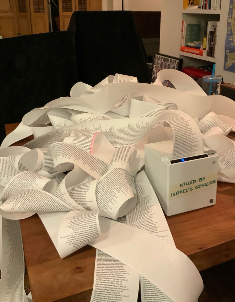 A receipt printer labeled “killed by Israel’s genocide” printing a long list of names into a pile on a table