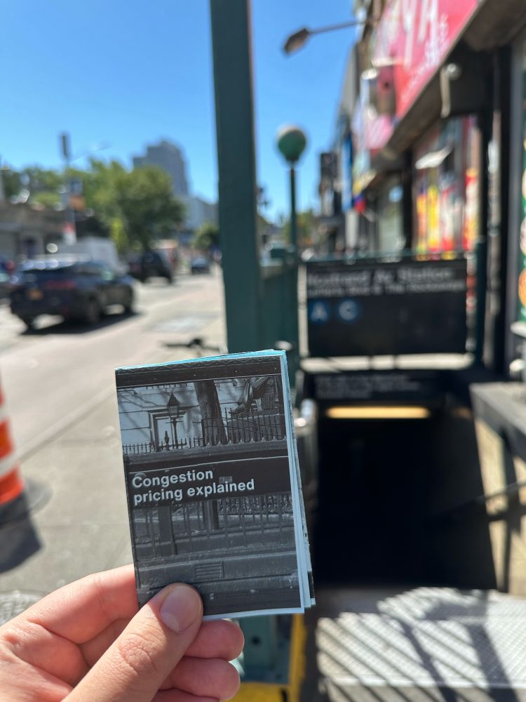 Holding a “Congestion pricing explained” zine at a subway station entrance