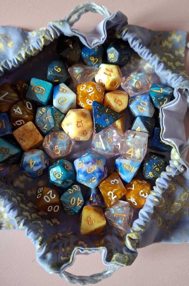 A photo of several dice sets for the boy, mainly in blue and gold, in a light purple dice bag