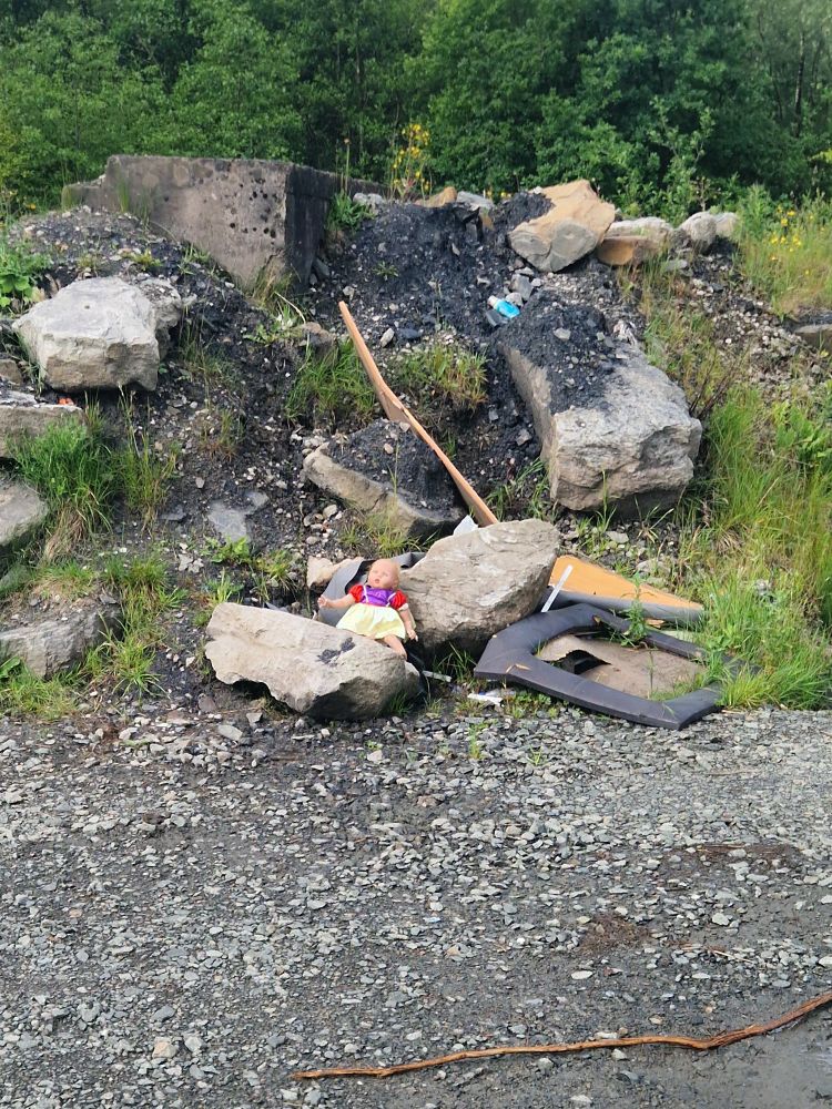 Flytipping in Falkirk with a creepy child's doll sitting on a rock surrounded  by rubbish.