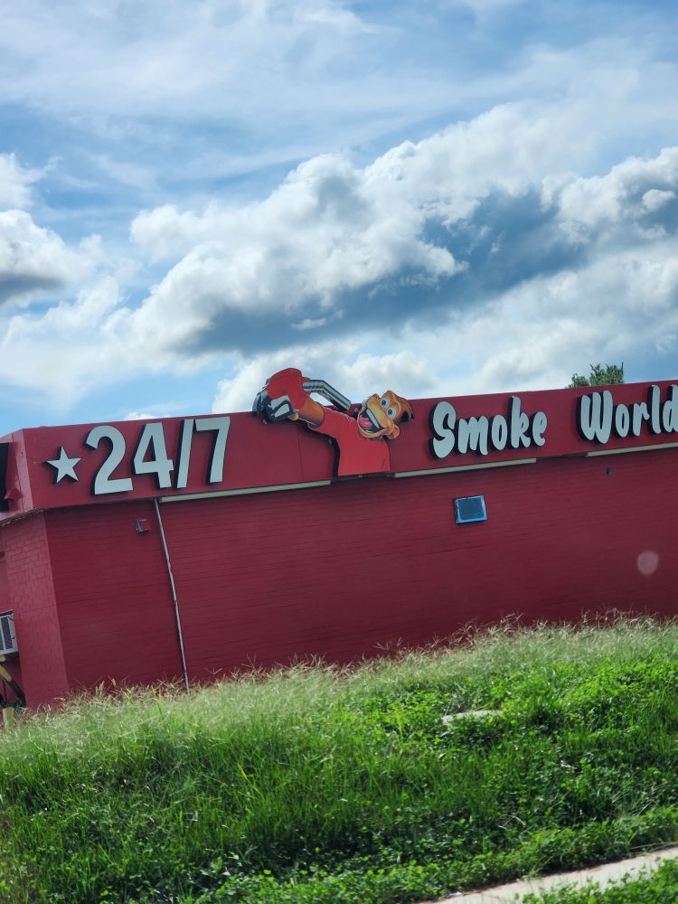 gas station that says 24/7 smoke world with a  cartoon monkey holding a gas pump at his mouth