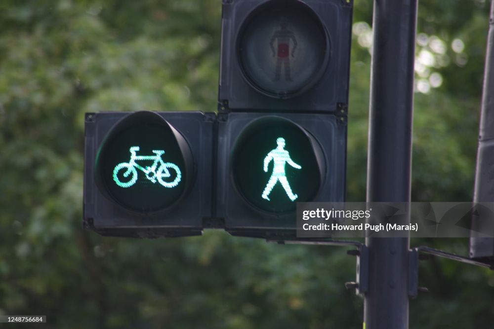 British pedestrian crossing signal with red standing person (turned off) and green bicycle & green walking person (turned on)