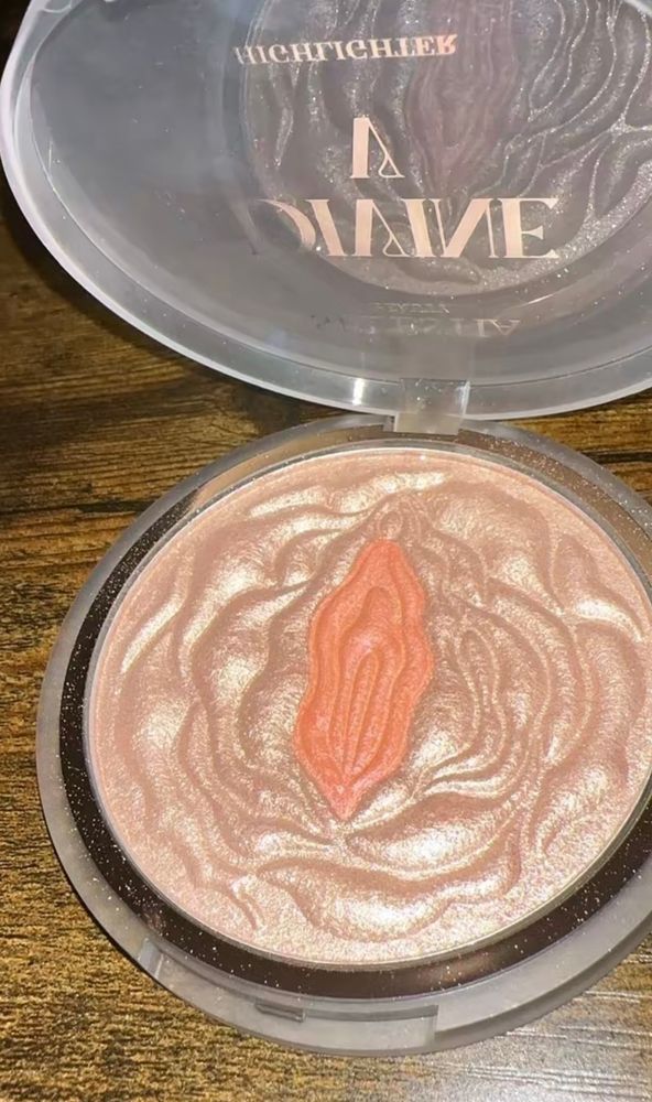 A makeup container of some sort of glittery highlighter powder or something and it’s peach colored but in the center is this clit-looking piece that looks even more peach. Colloquially it’s callled the glitter clitter