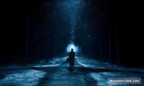 Screen cap from nosferatu where Nicholas holt stands in the middle of a wooded crossroads, silhouetted by a light in the distant middle. 