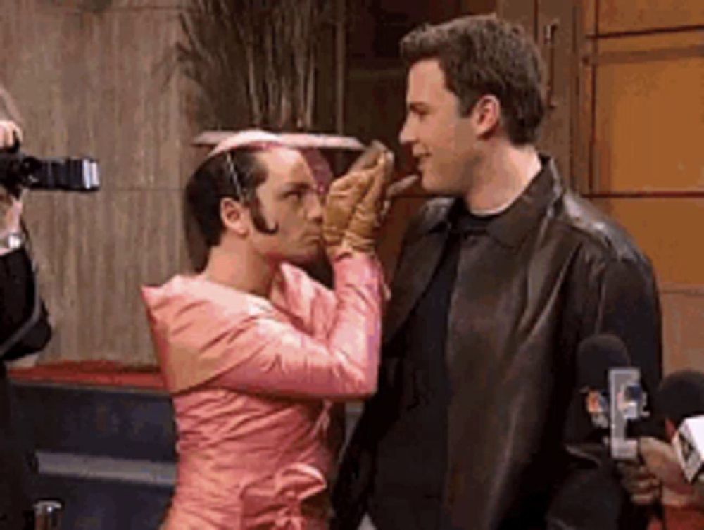 a man in a pink dress is touching the face of another man .