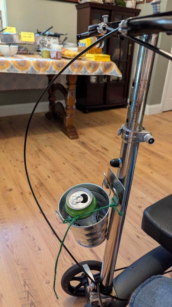 A knee scooter with a plant pot attached to the front with string and a can inside it