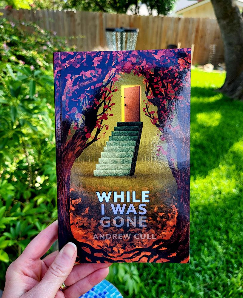 While I Was Gone by Andrew Cull

Cover shows a scene of trees with reddish leaves opening into a clearing with steps leading up to a door floating in air
