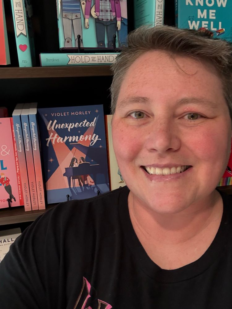 A Shelfy with me in the foreground with my book Unexpected Harmony in the background on a shelf with other books. Thanks to a new bookstore Eternal Endings that just opened in Snohomish. 