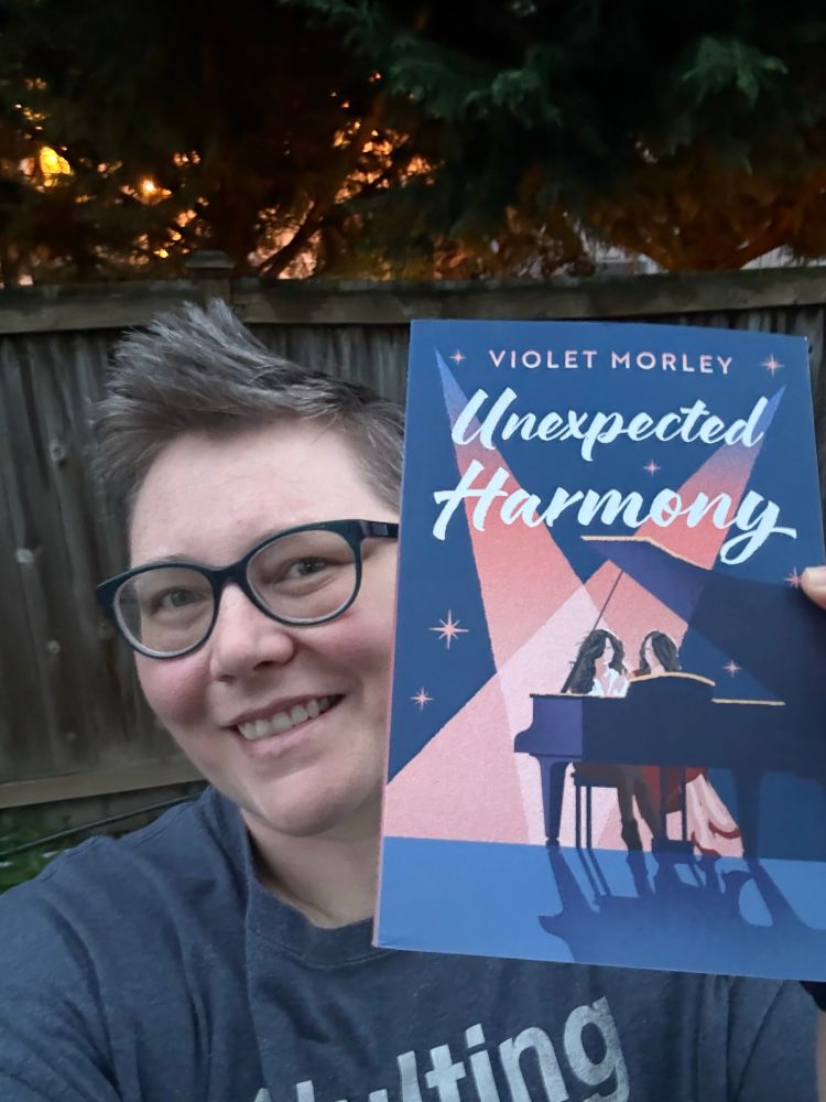 Author pic holding up book Unexpected Harmony with fence in the background. 