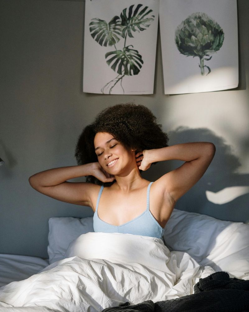 Woman waking up and stretching in a sunlit bedroom with botanical art decor.