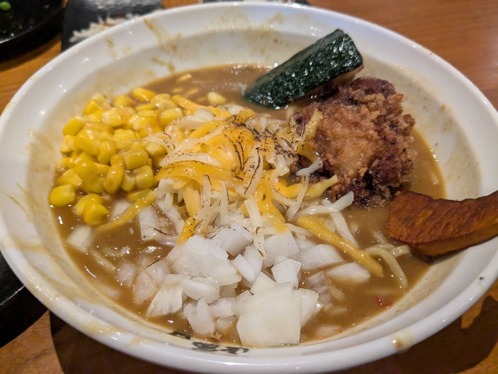 bowl of ramen with curry broth and topped with karaage chicken, zucchini, pumpkin, onions, corn and cheese 