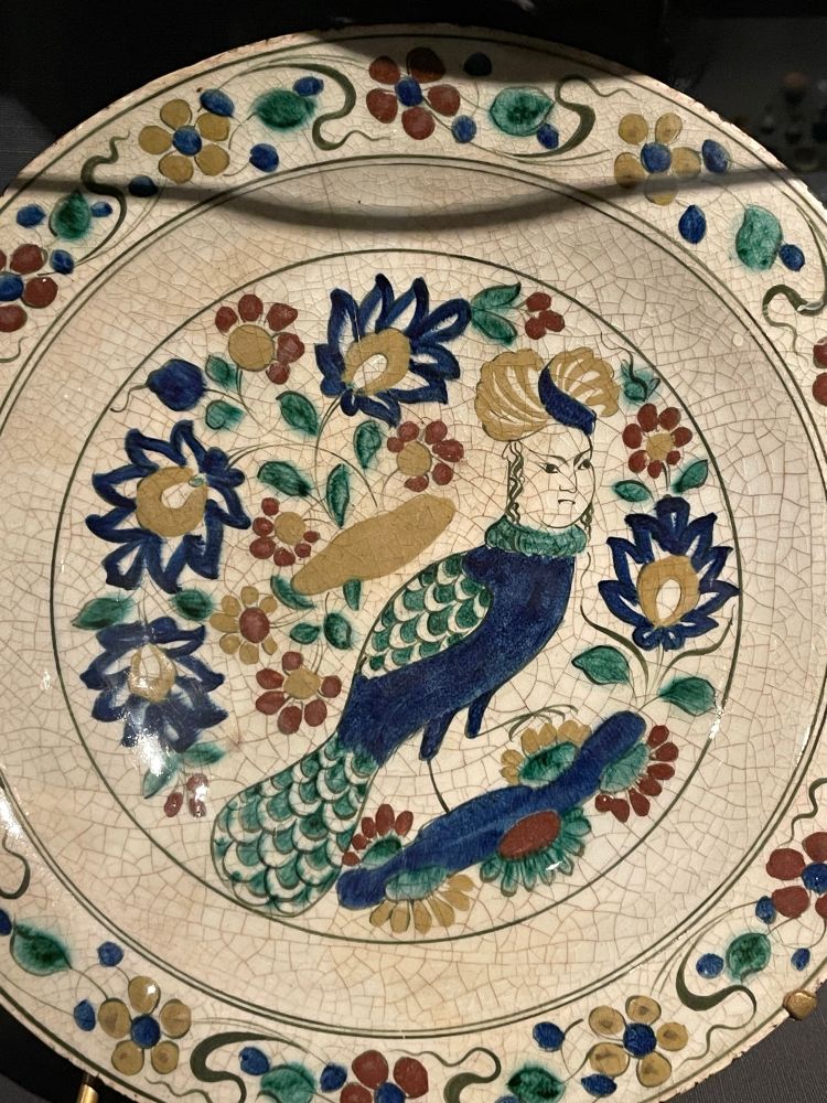 A little peacock dude with an angry dude’s head painted on a dish 