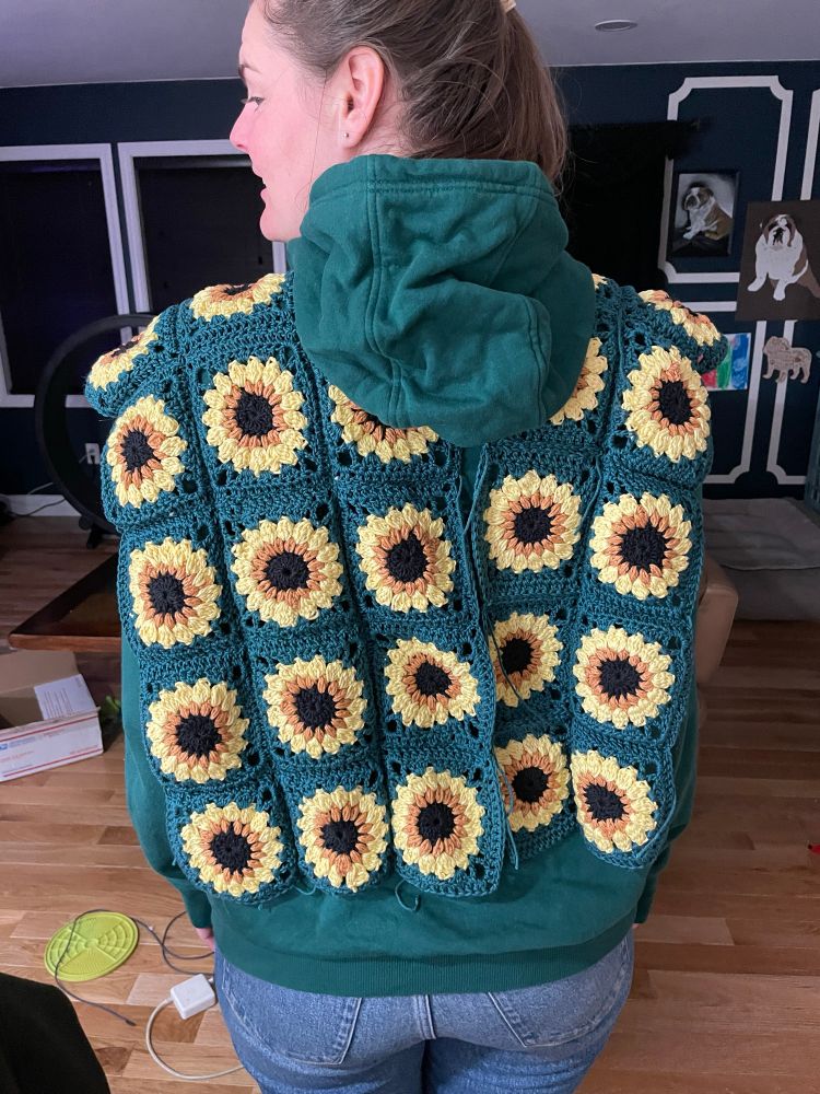 Back of Fiancée wearing a granny square sweater vest of sunflowers. It’s not quite connected at the back yet 