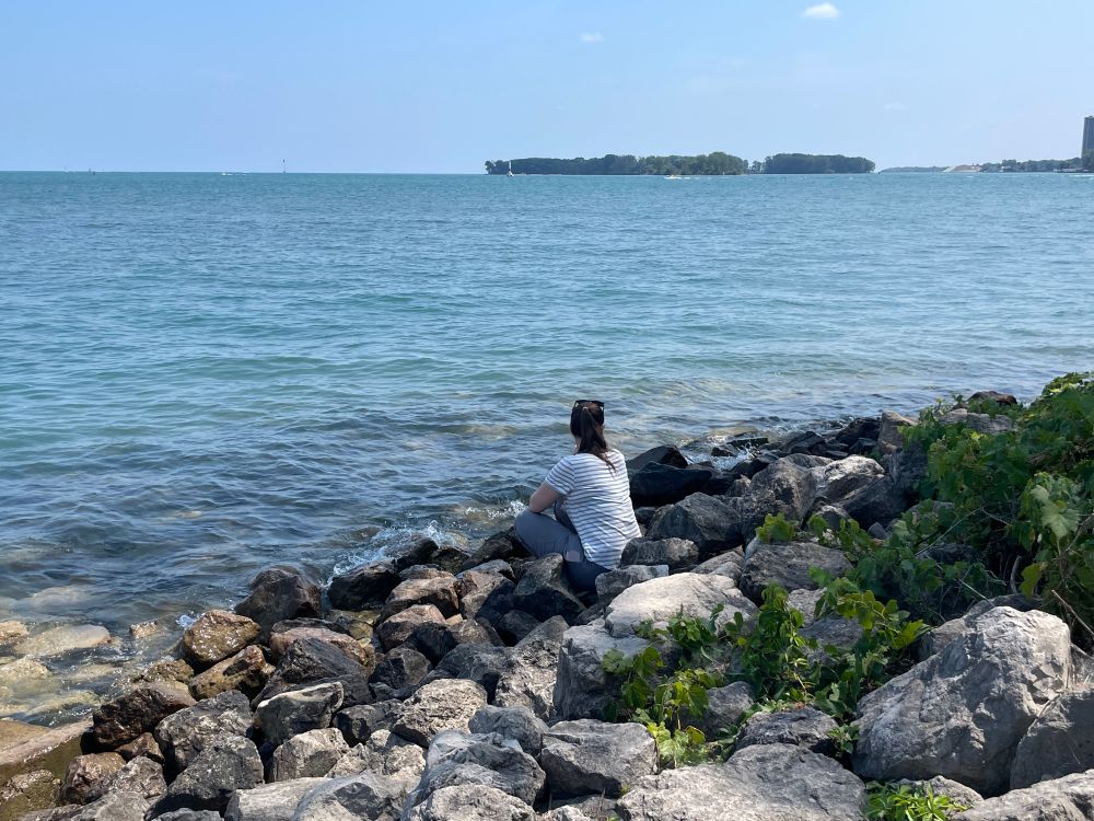 Fiancée sitting on rocks staring out over a body of water that leads to a Great Lake