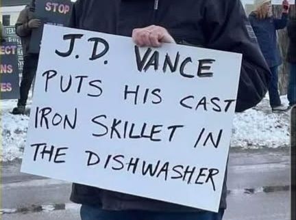 Handwritten placard reading "J.D. Vance puts his cast iron skillet in the dishwasher"