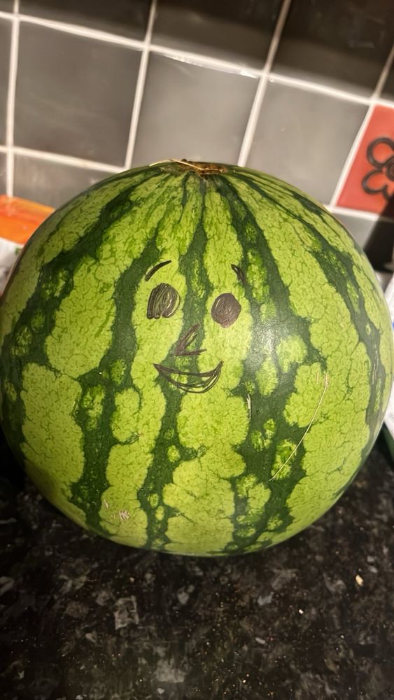 A watermelon with a smiley face drawn on in black sharpie 