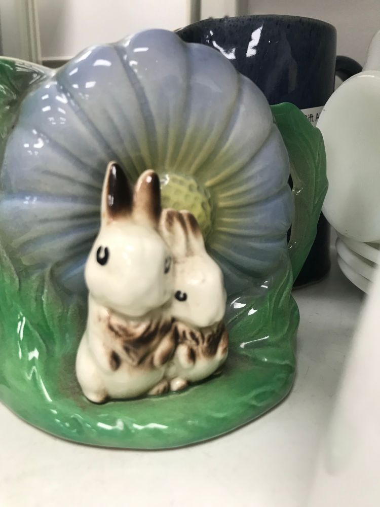 a trinket of two black and white rabbits sat on a grassy plain in front of a giant blue flower 