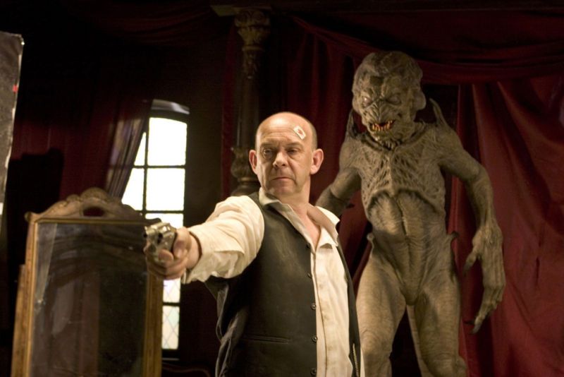 Doug Bradley aims a revolver off camera while Pumpkinhead stands behind him