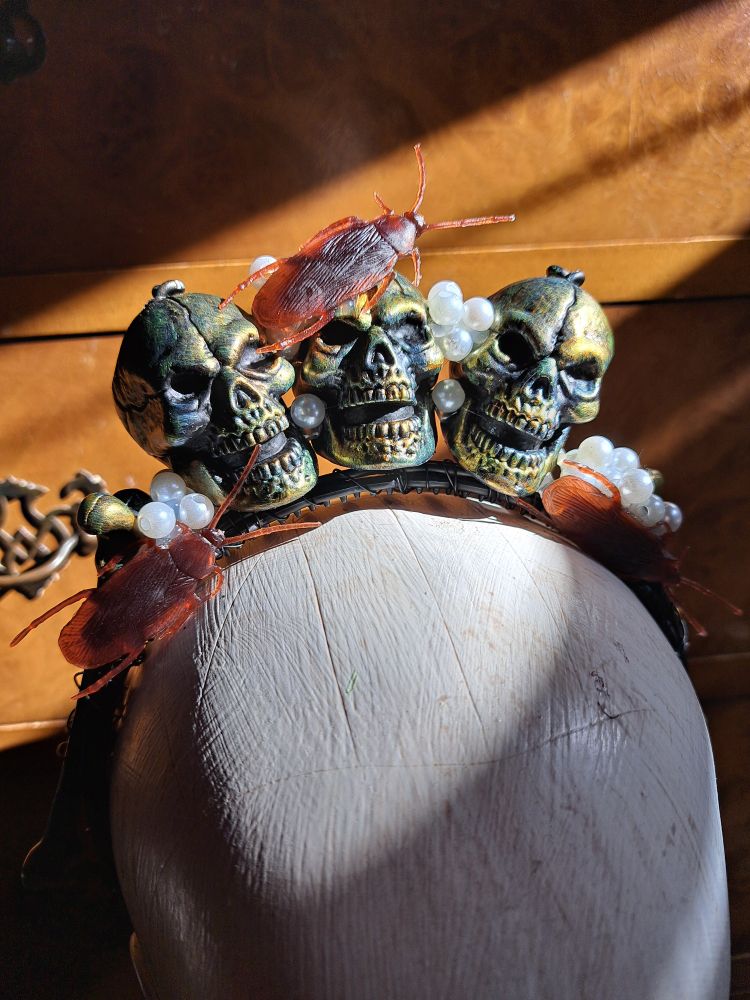 A crown with tarnished brass skulls roaches and roach egg pearls in the sunlight