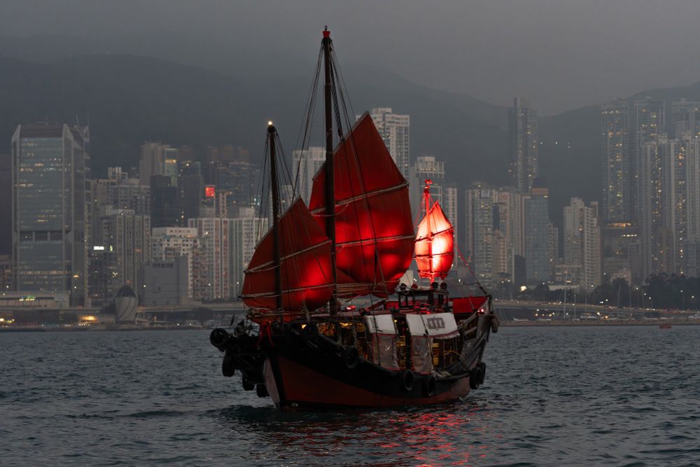 An illuminated junk boat in Victoria Harbour. Photographed from Kowloon, Hong Kong in the background.