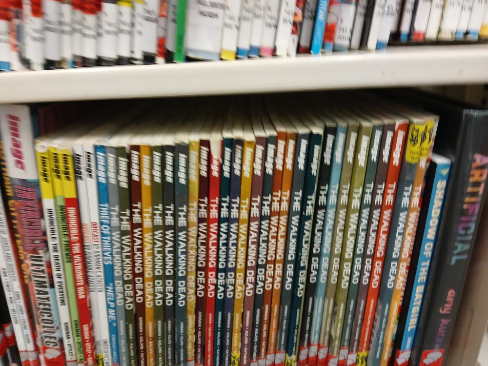 A photo of a library shelf with many volumes of Kirkman's "The Walking Dead. 