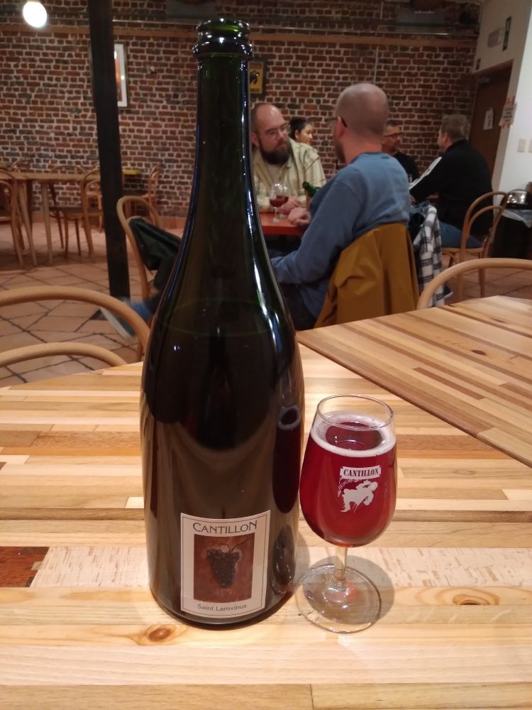 Magnum bottle of Saint Lamvinud with same beer in branded glass. Tasting room and fellow drinkers in background