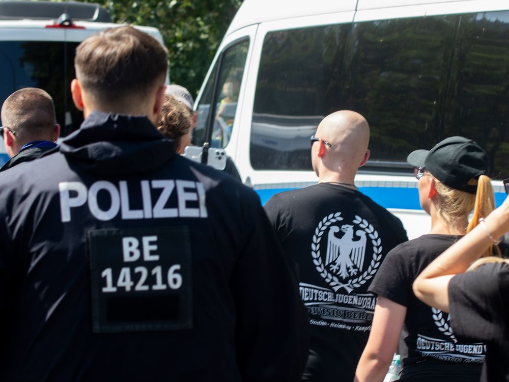 Zwei DJV-Mitglieder mit "Deutsche Jugend voran"-Shirts werden von der Polizei begleitet. (Symbolfoto)